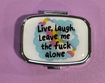 May include: A silver compact mirror with a white background and a rainbow design. The text on the mirror reads "Live, Laugh, Leave me the fuck alone."
