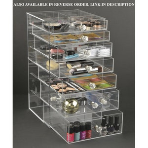 May include: Clear acrylic makeup organizer with seven drawers. The drawers are filled with various makeup products, including lipstick, eyeshadow, foundation, and nail polish.