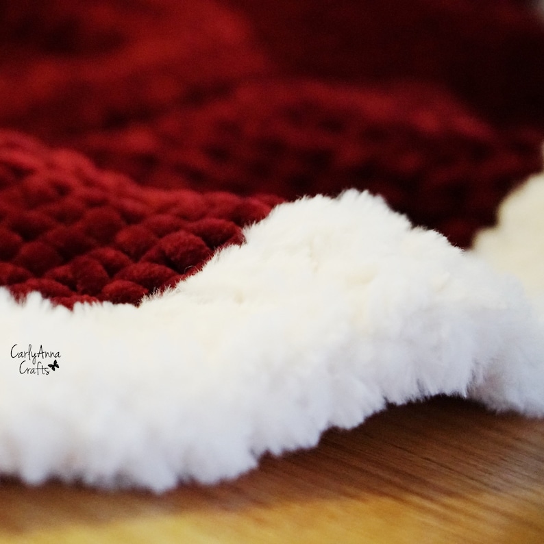 May include: A close-up of a red and white crocheted Christmas tree skirt. The skirt is made of a soft, fuzzy yarn and has a white faux fur trim.