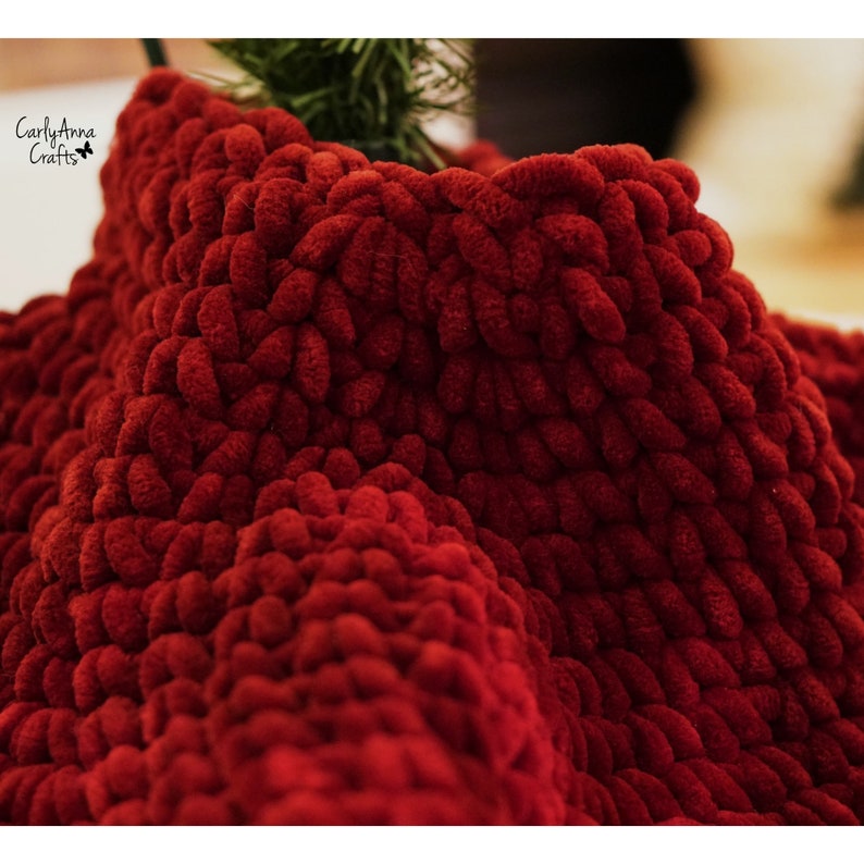 May include: Close-up of a deep red crocheted blanket with a soft, fuzzy texture. The blanket is made with thick yarn and has a unique, textured pattern.