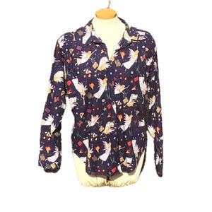 May include: A long-sleeved button-down shirt with a navy blue background and a repeating pattern of white angels, stars, and other celestial elements. The shirt has a classic collar and is displayed on a mannequin.