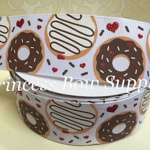 May include: White ribbon with a repeating pattern of donuts with chocolate and vanilla frosting, sprinkles, and red glitter hearts. The text "Princess Bow Supply" is printed on the ribbon.