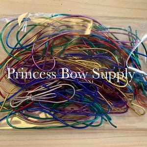 May include: A clear plastic bag filled with colorful metallic elastic cords. The cords are in various colors, including gold, silver, blue, green, red, and purple. The text "Princess Bow Supply" is printed on the bag.