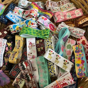 Pu&ograve; includere: Una collezione di nastri decorativi in un cesto di vimini. I nastri presentano vari motivi, tra cui cuori, pupazzi di neve e temi festivi. Alcuni nastri hanno testo, come "Valentine". I nastri sono di vari colori.