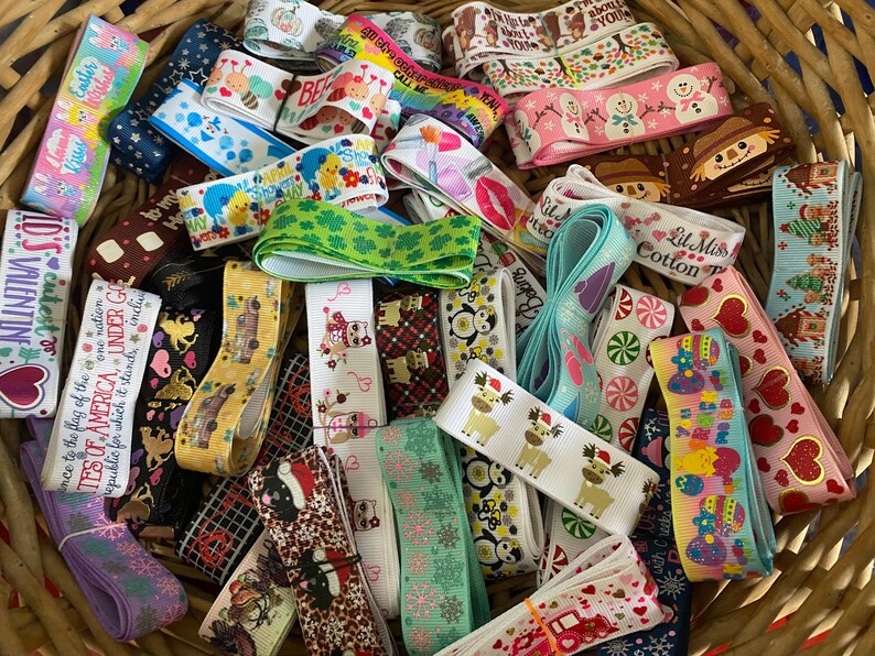 Pu&ograve; includere: Una collezione di nastri decorativi in un cesto di vimini. I nastri presentano vari motivi, tra cui cuori, pupazzi di neve e temi festivi. Alcuni nastri hanno testo, come "Valentine". I nastri sono di vari colori.