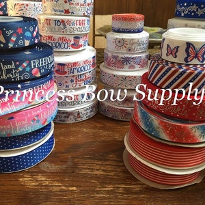 Pu&ograve; includere: Una collezione di nastri a tema patriottico in vari colori, tra cui rosso, bianco e blu. I nastri presentano disegni come stelle, strisce, fuochi d'artificio e testi come "Freedom" e "Little Miss America". Il testo "Princess Bow Supply" &egrave; anche visibile.