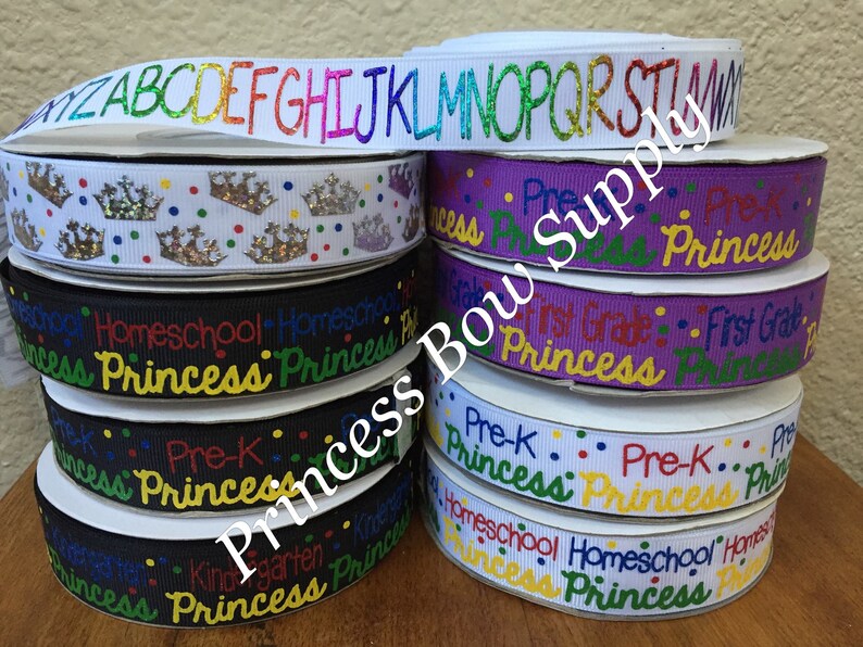 Pu&ograve; includere: Una pila di rotoli di nastro con vari disegni. Un rotolo presenta l'alfabeto in glitter arcobaleno, mentre altri mostrano corone, le parole "Homeschool Princess", "Pre-K Princess" e "First Grade Princess". I nastri sono di vari colori.