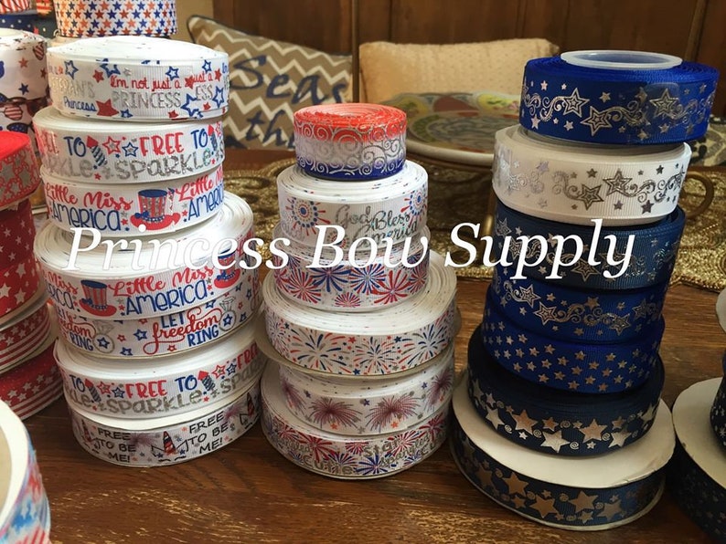 Pu&ograve; includere: Una collezione di nastri decorativi in vari colori e fantasie. Alcuni nastri presentano disegni patriottici con stelle, strisce e la scritta "Little Miss America". Altri nastri hanno motivi a stella metallici. Il testo "Princess Bow Supply" &egrave; visibile.