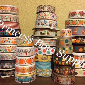 May include: A collection of fall-themed ribbon rolls with various patterns and colors, including orange, brown, green, and white. The ribbons feature designs such as pumpkins, owls, foxes, leaves, and the text "Give Thanks", "Hello Autumn", "Gobble", and "Fall is Here".