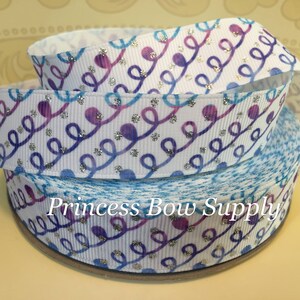 May include: White ribbon with a repeating pattern of blue and purple swirls and silver glitter accents. The ribbon is rolled up, with the text "Princess Bow Supply" visible on the bottom roll.