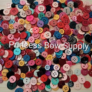 May include: A vibrant assortment of colorful buttons in various sizes and shades, including red, pink, blue, and yellow. The buttons are scattered, creating a visually appealing display. The text "Princess Bow Supply" is visible.
