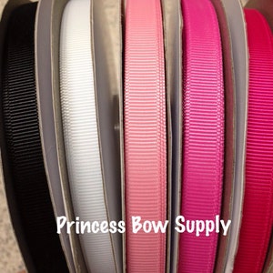 May include: A selection of grosgrain ribbon spools in various colors, including black, white, and shades of pink and red. The text "Princess Bow Supply" is visible on the packaging. Ideal for crafting and decorative projects.