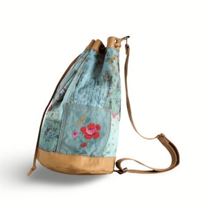 Op de afbeelding: Een blauwe en bruine patchwork-rugzak met een bloemenpatroon en leren accenten.