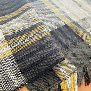 Peut inclure: Un chemin de table tissé avec un motif à carreaux noir, blanc et jaune. Le chemin de table a une bordure frangée.