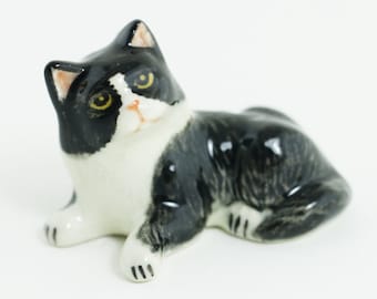 May include: A black and white ceramic figurine of a cat lying down. The cat has yellow eyes and a black nose.