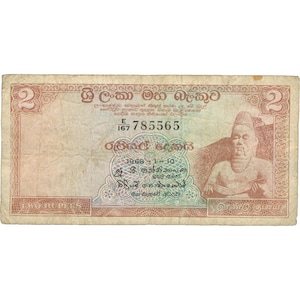 Puede incluir: Un billete de dos rupias de Sri Lanka, con un retrato de un hombre con ropa tradicional y el texto "ශ්‍රී ලංකා මහ බැංකුව" en escritura cingalesa. El número de serie es E 167 785565.
