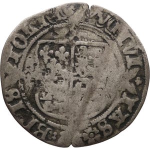 May include: A worn silver coin with a central emblem, possibly a coat of arms, and surrounding text. The coin's surface shows signs of age and wear, with visible imperfections and edge damage.