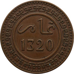 May include: A copper coin with a decorative border and the year 1320 in Arabic numerals. The coin also features the Arabic word "One" in the center.