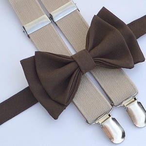 May include: A set of beige suspenders with brown bow tie. The suspenders have silver clips and the bow tie is made of a soft fabric.