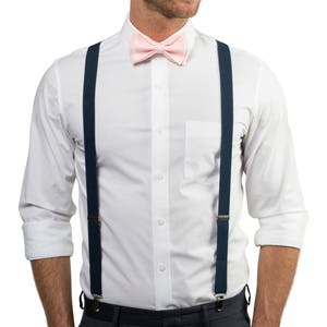 May include: A white dress shirt with a pink bow tie and navy blue suspenders.