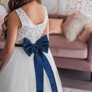 Back of girl in a white navy beaded dress with a navy bow