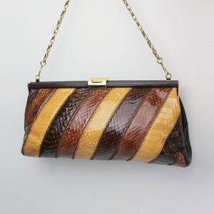 May include: A vintage clutch bag with a gold chain strap. The bag has a striped pattern in shades of brown and tan, with a gold clasp. The rectangular bag appears to be made of leather or a similar material.