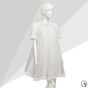 Könnte beinhalten: Ein weißes Nachthemd im Vintage-Stil mit kurzen Ärmeln und einer ausgestellten Silhouette. Das Nachthemd hat zarte Spitzenbesätze am Saum und an den Ärmelrändern sowie kleine rosa Blumenakzente am Halsausschnitt. Das Kleidungsstück wird auf einer Schaufensterpuppe präsentiert.