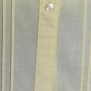 Puede incluir: Primer plano de una tela de color amarillo claro con rayas verticales. La tela tiene una textura sutil y una apariencia ligeramente transparente.