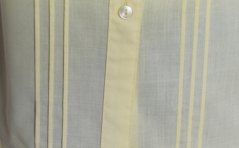 Puede incluir: Primer plano de una tela de color amarillo claro con rayas verticales. La tela tiene una textura sutil y una apariencia ligeramente transparente.