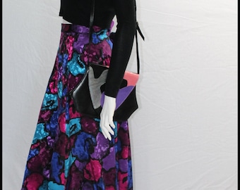 May include: A black long-sleeved top with a colorful, abstract print skirt. The skirt has a high waist and a flowing silhouette. A black crossbody bag with a colorful geometric design is worn over the top.