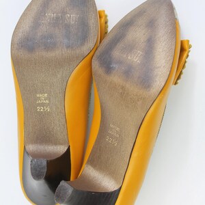 May include: A pair of yellow leather pumps with a pointed toe and small heel. The soles are worn and show the text "MADE IN JAPAN" and the size "22 1/2". The heels are dark brown.