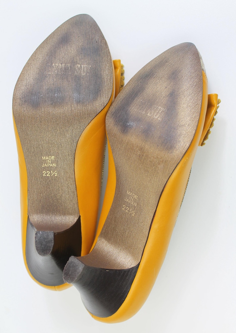 May include: A pair of yellow leather pumps with a pointed toe and small heel. The soles are worn and show the text "MADE IN JAPAN" and the size "22 1/2". The heels are dark brown.