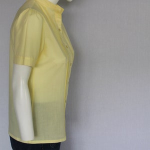 Puede incluir: Una camisa amarilla de manga corta con botones y cuello mandar&iacute;n.