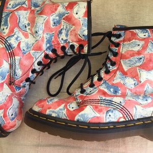 Op de afbeelding: Paar enkellaarsjes met een rood en blauw vispatroon. De laarzen hebben zwarte veters, een zwarte zool en gele stiksels. De laarzen zijn gemaakt van een duurzaam materiaal.