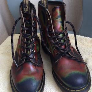 Könnte beinhalten: Ein Paar Stiefeletten mit einem einzigartigen, farbenfrohen Design. Die Stiefel weisen eine Mischung aus roten, grünen und schwarzen Farbtönen auf, mit schwarzen Schnürsenkeln und Ösen. Die Sohlen sind schwarz mit gelben Nähten. Der Text "WITH BOUNCING SOLES" ist sichtbar.