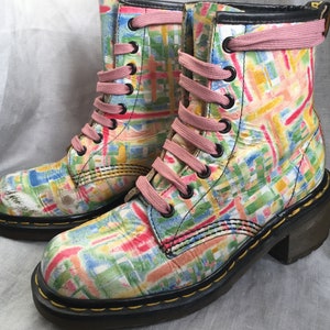 Op de afbeelding: Een paar kleurrijke enkellaarsjes met een geometrisch patroon in roze, blauw, groen en geel. De laarzen hebben roze veters, zwarte vetergaten en een zwarte zool met een kleine hak. De laarzen zijn van leer.