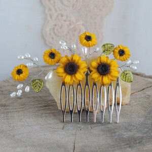 May include: A silver hair comb with a floral design featuring yellow sunflowers and white pearl accents. The comb is decorated with green leaves and is perfect for adding a touch of whimsy to any hairstyle.