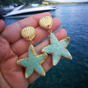 K&ouml;nnte beinhalten: Ein Paar goldene und hellblaue Ohrringe mit einem Muschel- und einem Seestern-Anh&auml;nger.