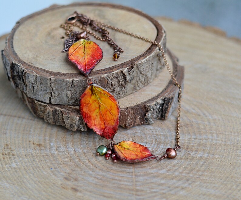 May include: A necklace with three orange, yellow, and red leaves, accented with copper wire and small green and brown beads.