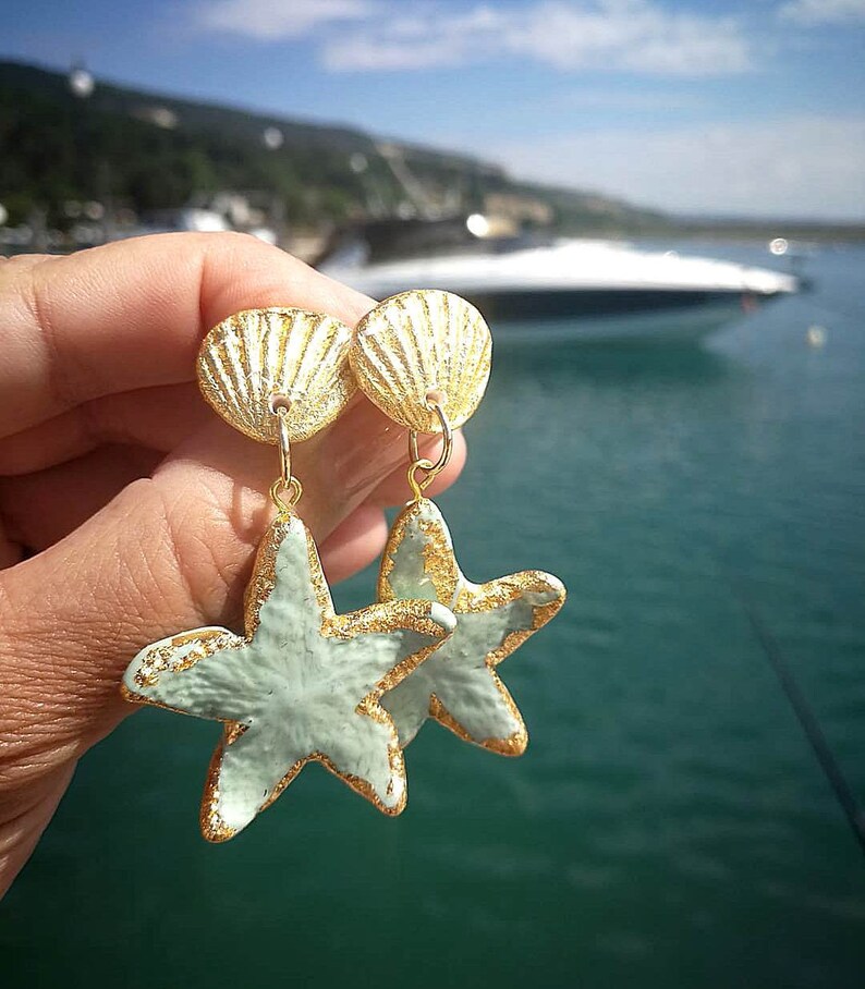 K&ouml;nnte beinhalten: Goldene und hellblaue Seestern-Ohrringe mit einem goldenen Muschel-Anh&auml;nger. Die Ohrringe sind handgefertigt und haben einen zarten, femininen Look.