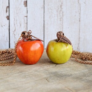 May include: Two apple-shaped pendants on gold chains. The apple on the left is red and the apple on the right is green.