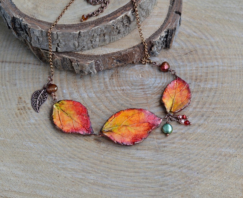 May include: A copper chain necklace with three orange, red, and yellow leaves, accented with copper wire, beads, and a small leaf charm.