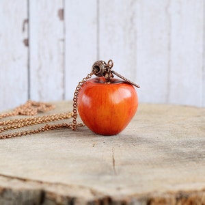May include: A red apple pendant necklace with a copper chain. The apple is a realistic-looking, hand-crafted piece of jewelry.