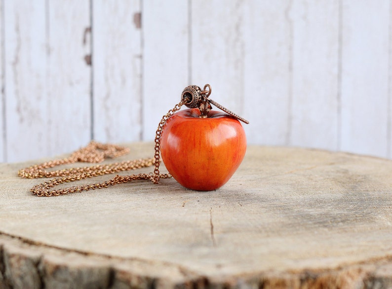 May include: A red apple pendant necklace with a copper chain. The apple is a realistic-looking, hand-crafted piece of jewelry.