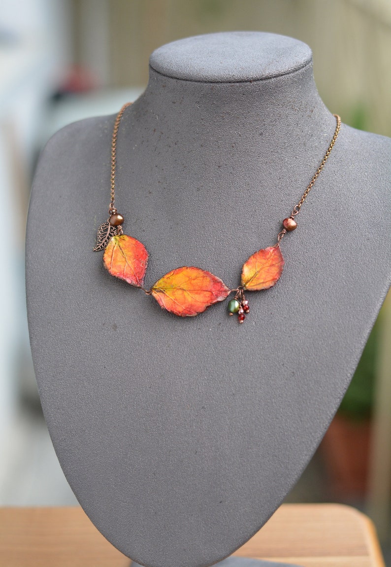 May include: A copper chain necklace with three orange, red, and green leaves, and small red and green beads.