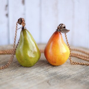 May include: Two pear-shaped pendants on gold chains. One pear is green and the other is yellow. Both have a small metal detail at the top.