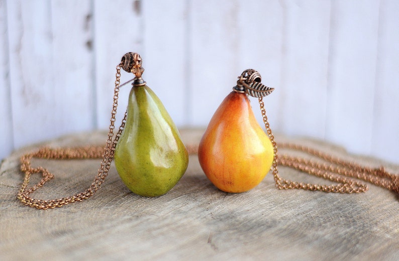 May include: Two pear-shaped pendants on gold chains. One pear is green and the other is yellow. Both have a small metal detail at the top.