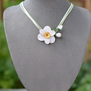 May include: A white and yellow paper flower necklace with green leaves. The necklace is on a grey mannequin bust.