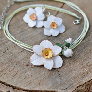 May include: A white and green necklace and earrings set featuring delicate polymer clay daffodils. The necklace has a multi-strand design with a large daffodil pendant and two smaller buds.