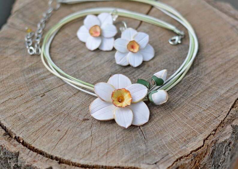 May include: A white and green necklace and earrings set featuring delicate polymer clay daffodils. The necklace has a multi-strand design with a large daffodil pendant and two smaller buds.